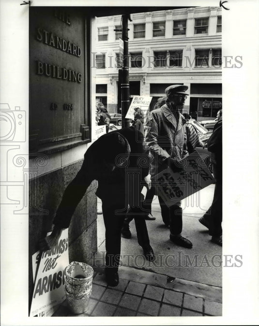 1985 Press Photo A late arrival picks up his sign as a 100 others march protest- Historic Images