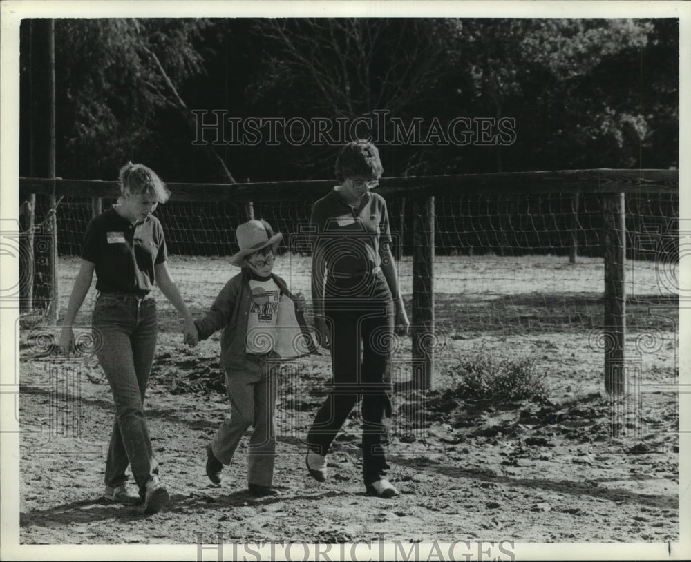 1983 Press Photo Child walks with volunteers along fence at ranch in Texas- Historic Images