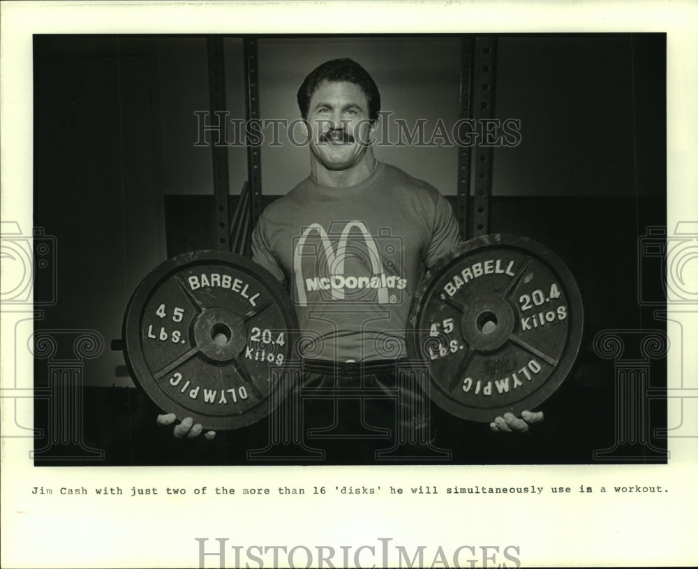 1985 Press Photo Weightlifter Jim Cash holds two 45 pound barbell disks.- Historic Images