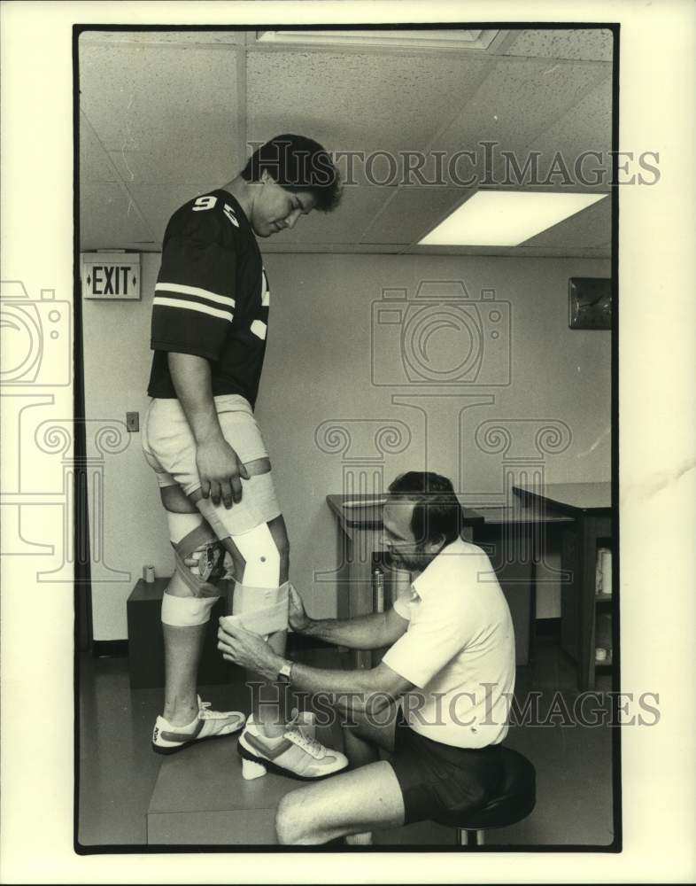 1983 Press Photo Rice trainer Allen Eggert puts knee brace on Joe Rios.- Historic Images