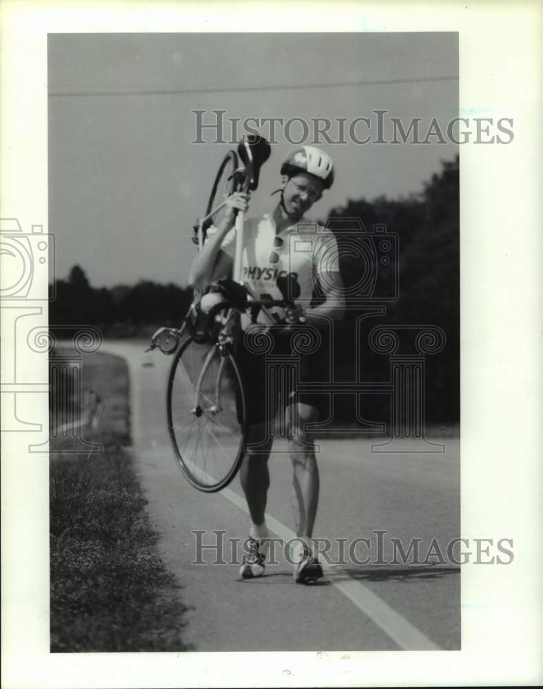 1989 Press Photo Bicycle racer Rick Kent carries his bike along the road- Historic Images