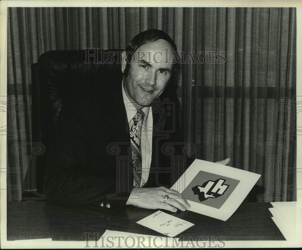 1974 Press Photo Chuck Rohe sits at his desk holding Texas sports team emblem- Historic Images