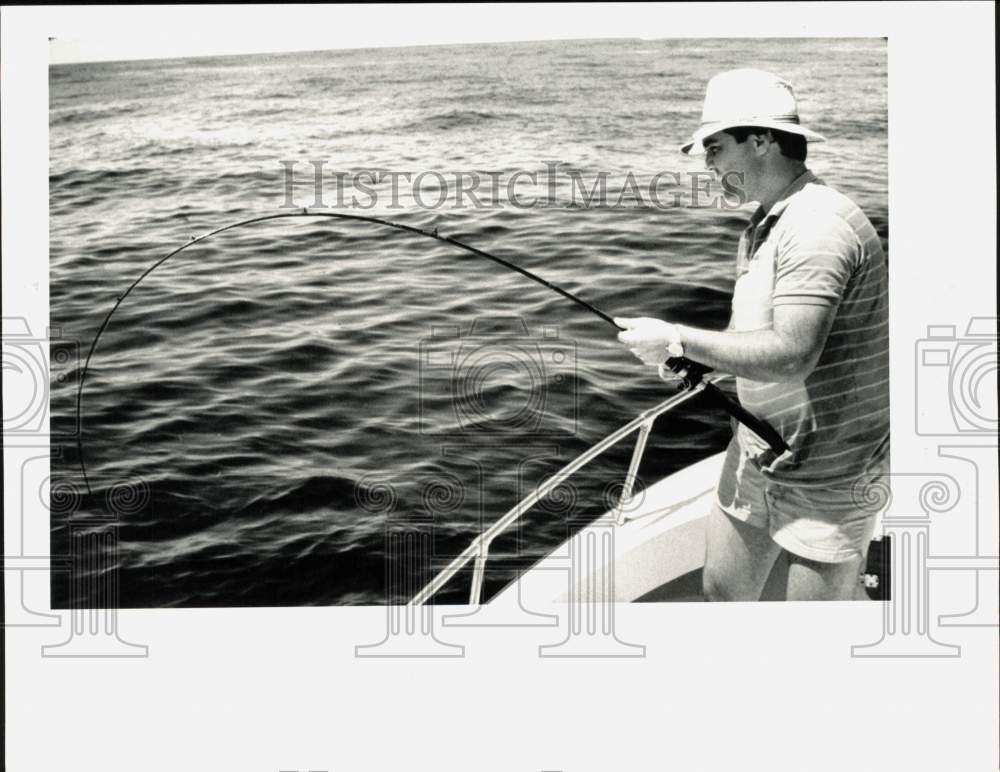 1985 Press Photo Man pulls in fish while standing on fishing boat. - hpa28901- Historic Images