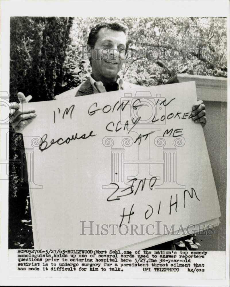 1965 Press Photo Comedy writer Mort Sahl holds card to press in Hollywood- Historic Images