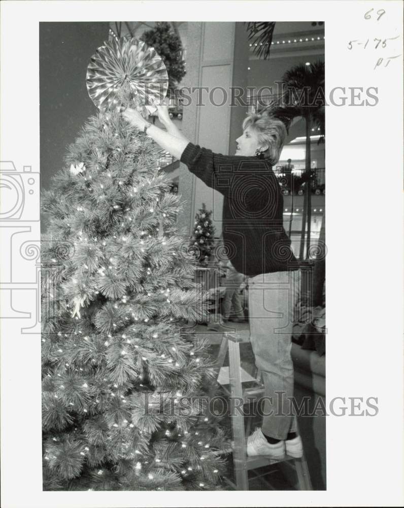 Press Photo A woman standing on ladder to place Christmas tree topper.- Historic Images