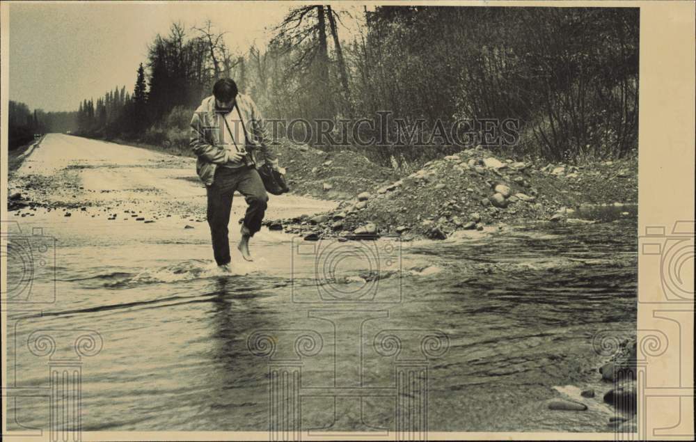 1986 Press Photo Man walks barefoot through flood water running across the road- Historic Images