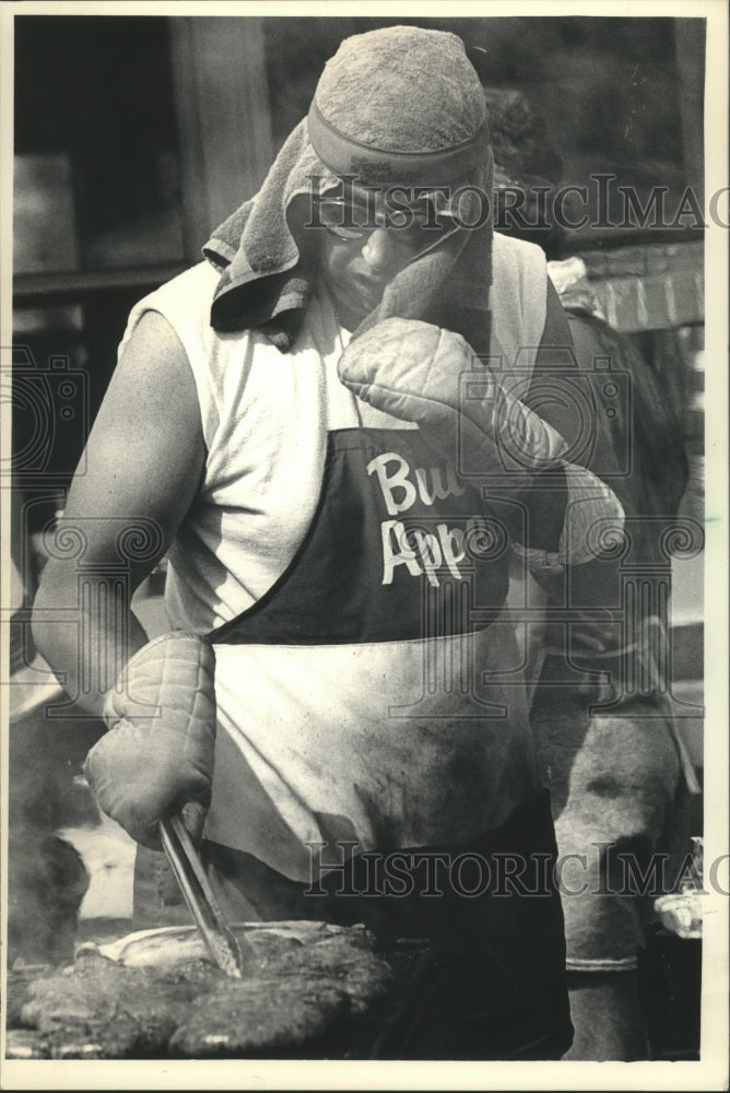 1987 Press Photo John Dooley protecting himself from heat while cooking sausages- Historic Images