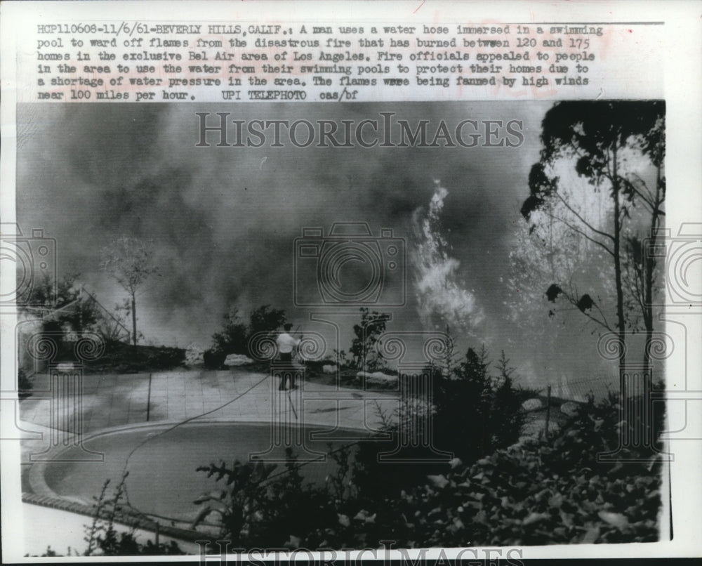 1961 Press Photo Man uses Water Hose from Swimming Pool to Keep Flames at Bay- Historic Images