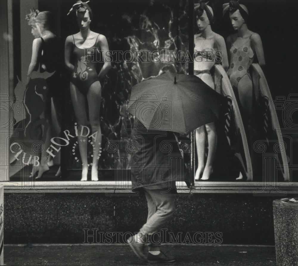 1990 Press Photo Pedestrian fights rain passed window of bathing suits-Milwaukee- Historic Images