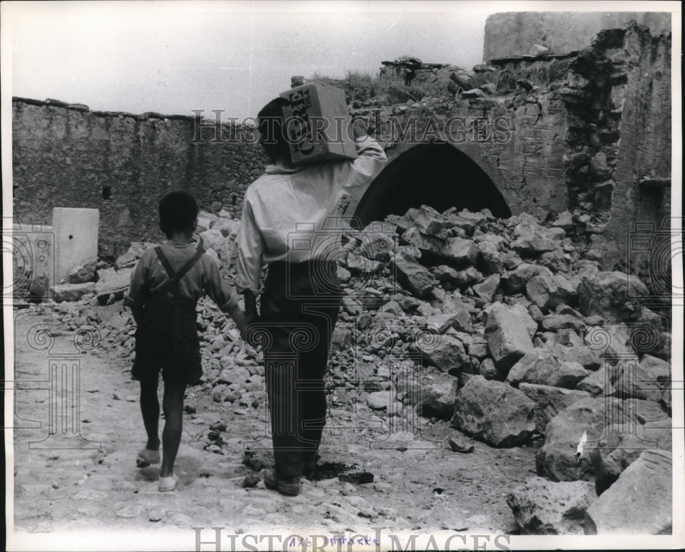 1964 Press Photo Greek Father &amp; Son Traverse Earthquake Rubble with CARE Package- Historic Images