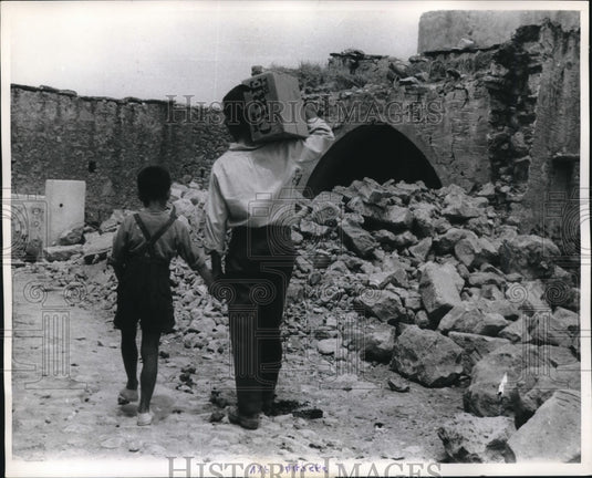 1964 Press Photo Greek Father & Son Traverse Earthquake Rubble with CARE Package- Historic Images