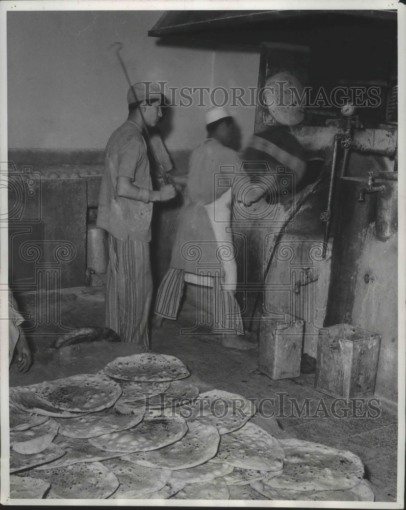 1956 Press Photo Baker tosses dough into oven, fresh-baked bread cools on floor- Historic Images