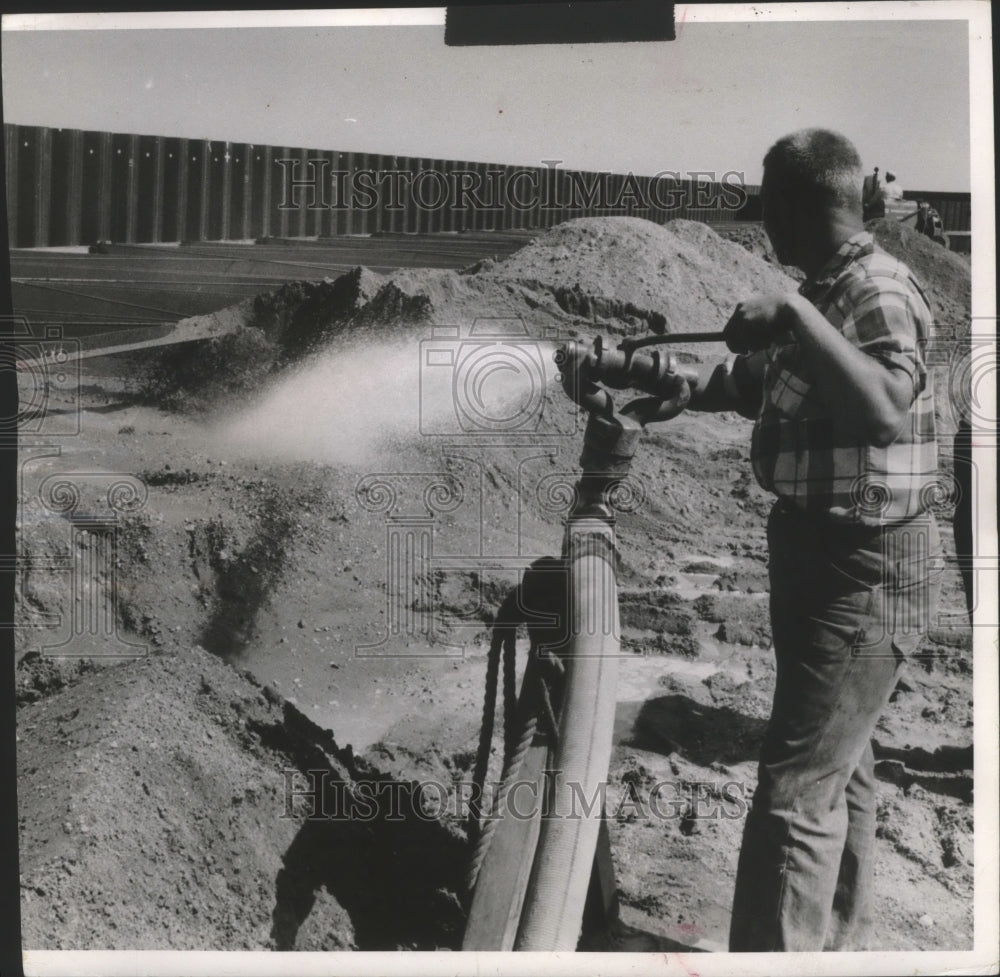 1958 Press Photo Worker sprays water on gravel fill dumped at Milwaukee Harbor