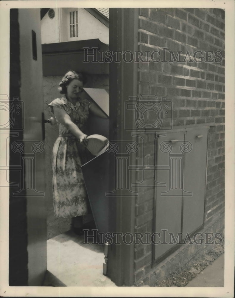 1952 Press Photo Woman places trash and garbage into a bin from inside house