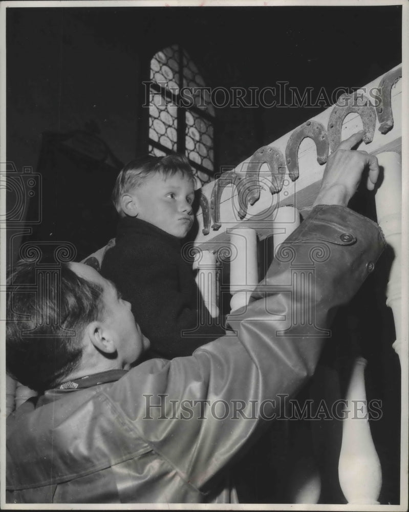 Load image into Gallery viewer, 1955 Press Photo Boy and man looking at horseshoes in a church in Germany
