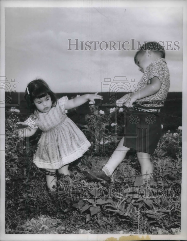 1959 Press John Sommers helps his two year old sister Carolyn over barb wire in