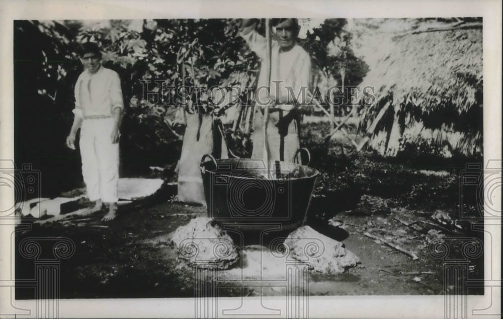 1940 Press Photo Two Men Shown Bringing Large Pot to Boil Over Fire