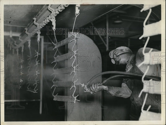 1931 Press Photo Spray painter paints metal parts on endless belt chain