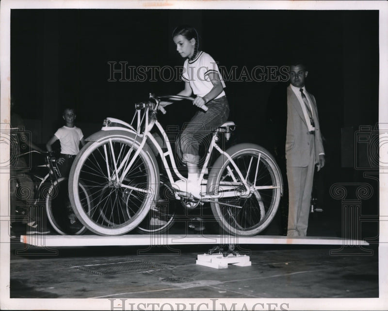 Load image into Gallery viewer, 1955 Press Photo Jacqueline Kaeperski crossing obstacle course on her bicycle
