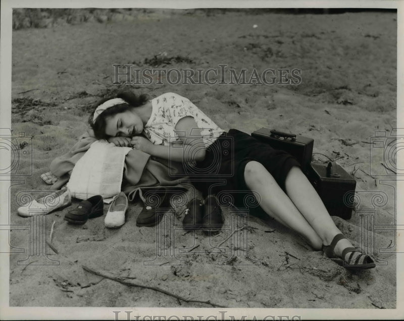 Load image into Gallery viewer, 1947 Press Photo Girl Sleeping Atop Luggage, Clothing on Sand - nee22585
