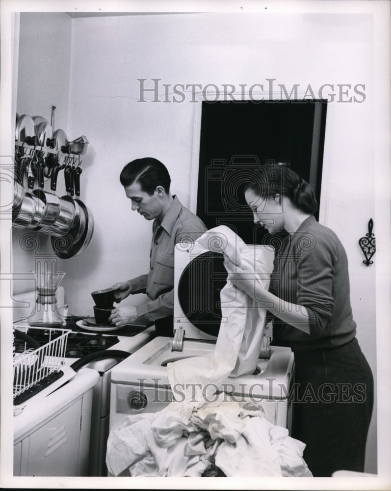 Press Photo A man and woman doing laundry and dishes. - nee48668