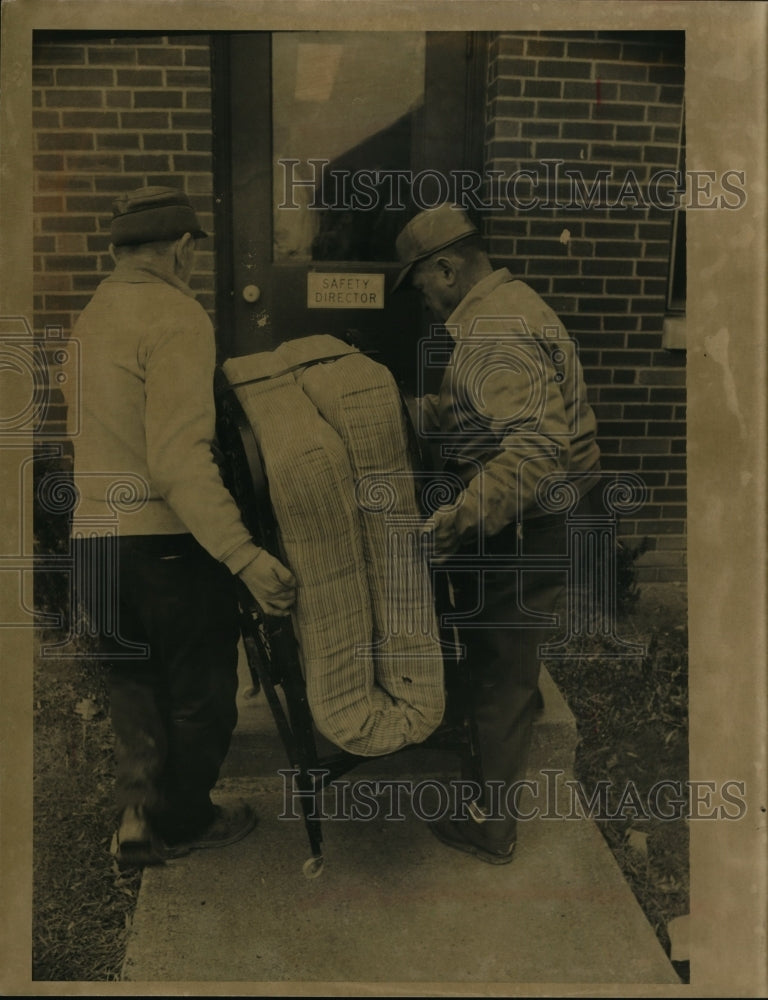Press Photo Two men move a foldaway mattress into a building - nef36601
