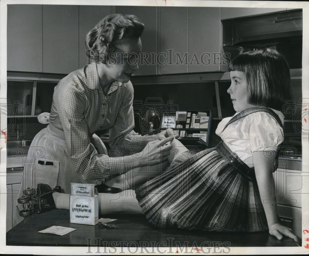 1958 Press Photo Woman bandages daughters knee with sterile gauze