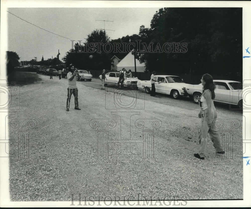 1977 Press Photo String of cars with onlookers and couple tossing a ball.- Historic Images