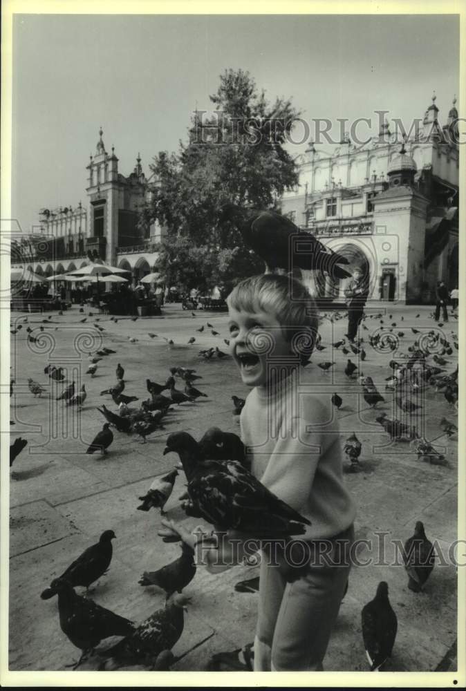 1988 Press Photo Young boy feeding pigeons on Main Market Square- Krakow, Poland- Historic Images