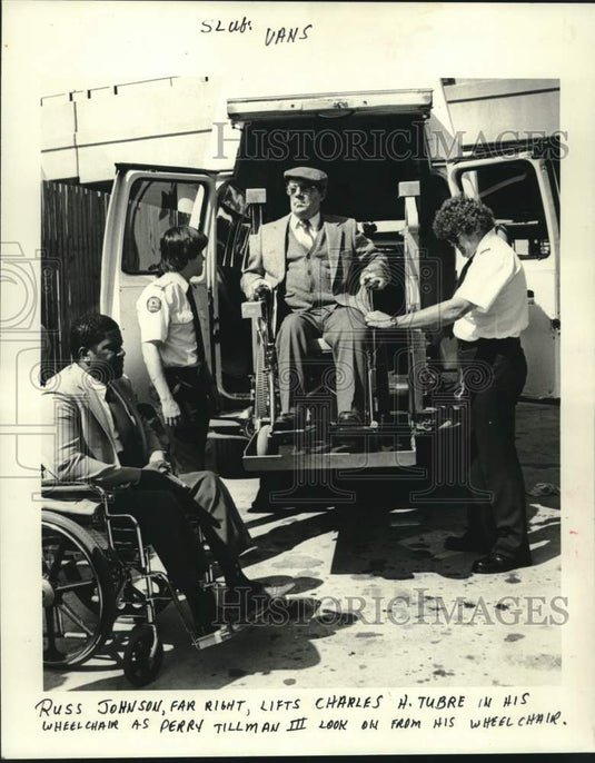 1985 Press Photo Russ Johnson lifts Charles Tubre in his wheelchair into a van.