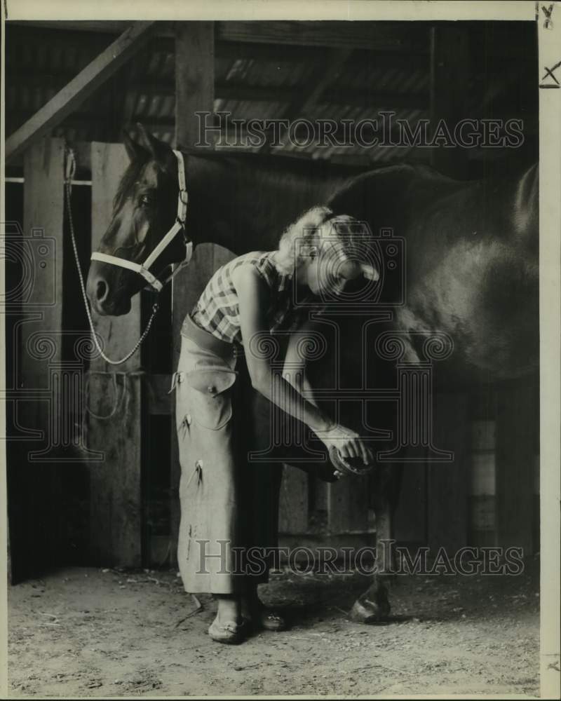 1956 Press Photo Kathlyn &quot;Chickie&quot; Younger cleans hoofs of Chico Beau at stables- Historic Images