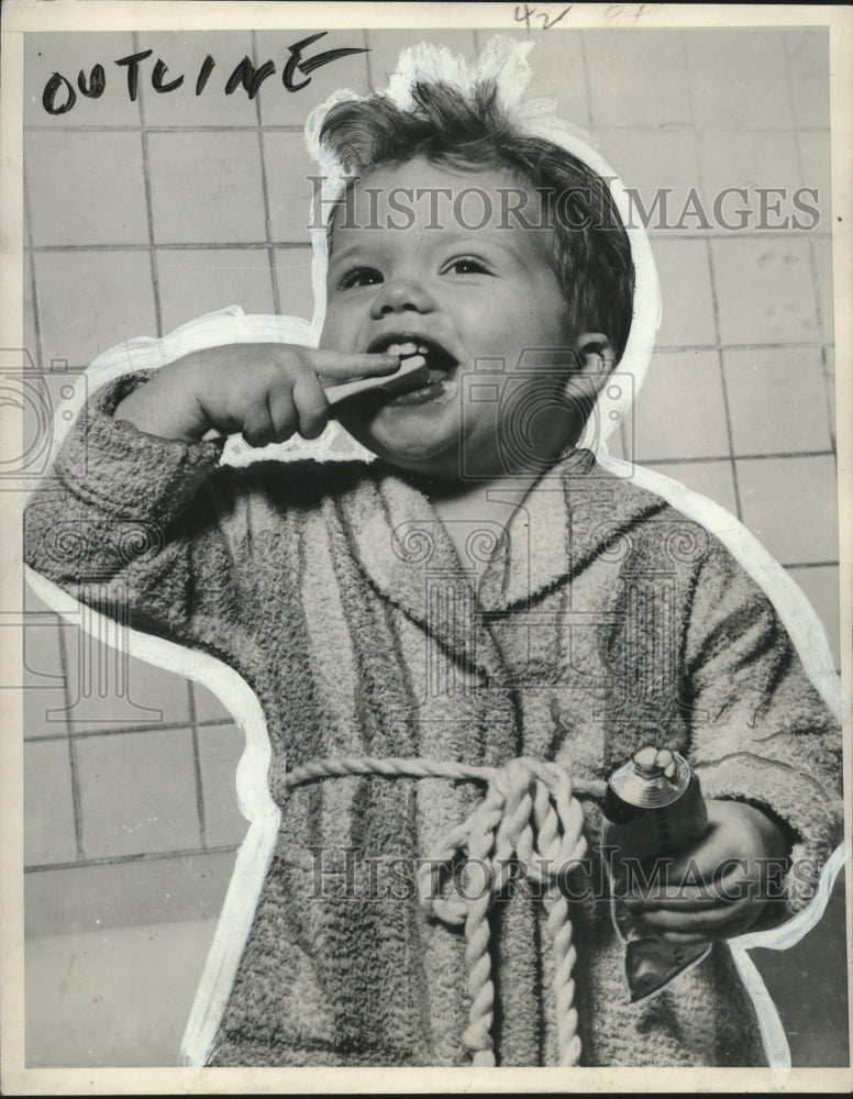 1952 Press Photo Child in bathrobe brushing teeth and holding tube of toothpaste