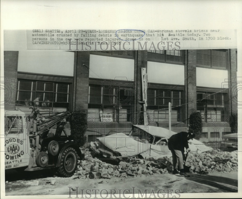 1965 Press Photo Workman shovels near crushed automobile by earthquake debris
