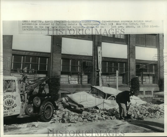 1965 Press Photo Workman shovels near crushed automobile by earthquake debris
