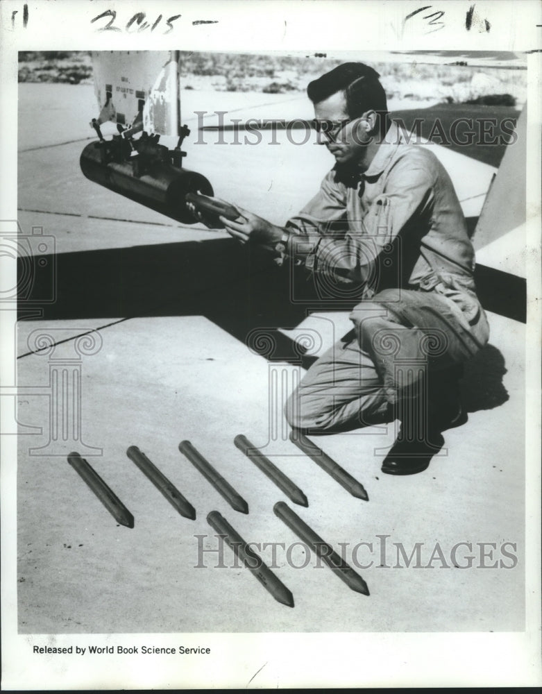 1969 Press Photo Dr. Sinclair loads "seeds" under jet wing to target hailstorms