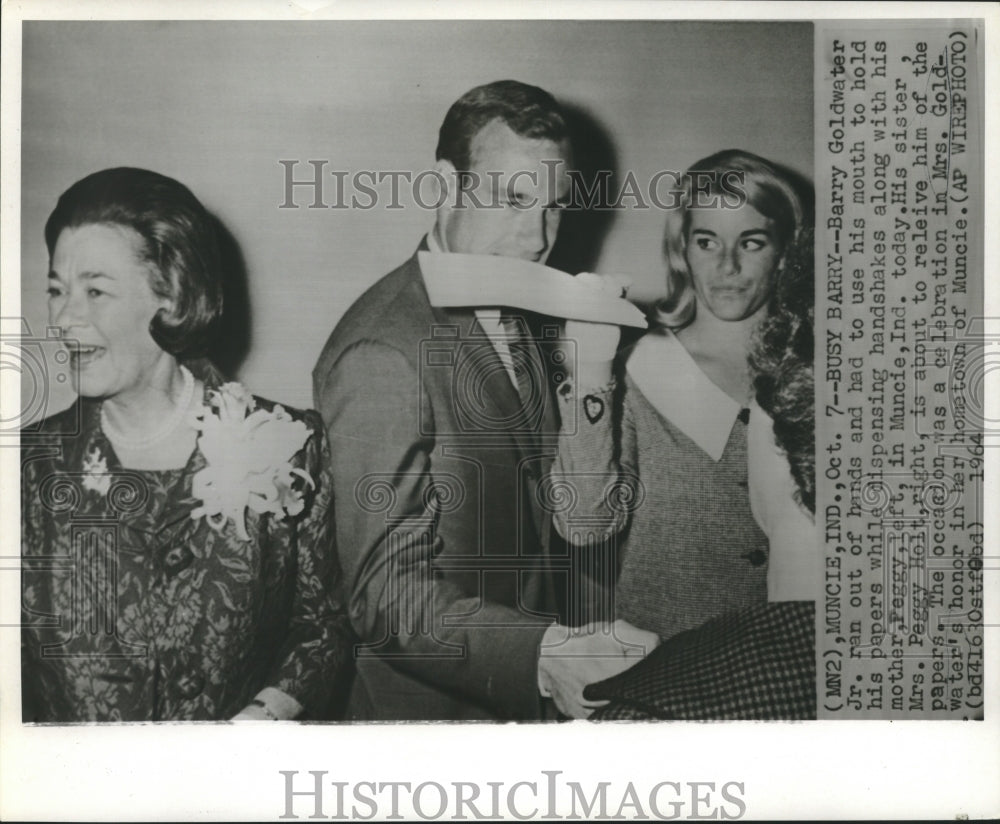 1964 Press Photo Barry Goldwater, Jr., used his mouth to hold paper, shake hands