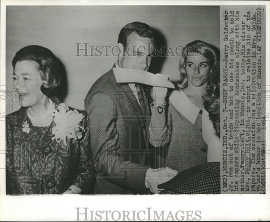 1964 Press Photo Barry Goldwater, Jr., used his mouth to hold paper, shake hands
