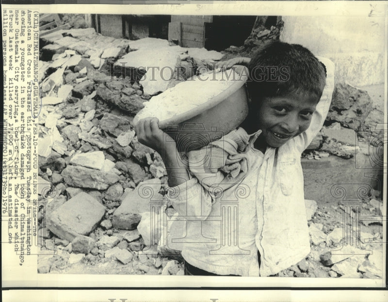 Load image into Gallery viewer, 1976 Press Photo Guatemalan boy carries bowl of flour amidst earthquake rubble

