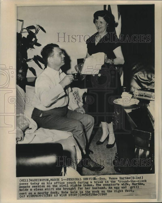 1960 Press Photo Senator Hartke rests on office couch as wife brings clean shirt