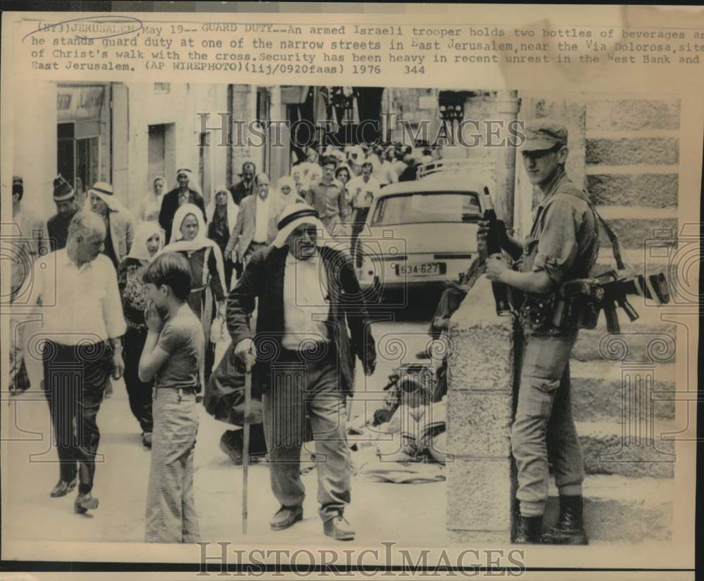 1976 Press Photo Israeli trooper hold two beverages while standing Guard Duty.