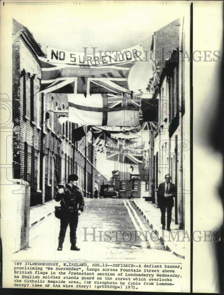 Load image into Gallery viewer, 1971 Press Photo Defiant banner hangs over street guarded by English soldier
