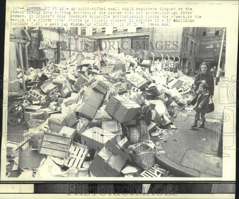Load image into Gallery viewer, 1970 Press Photo Child and mother pass rotting rubbish on London's Peter Street
