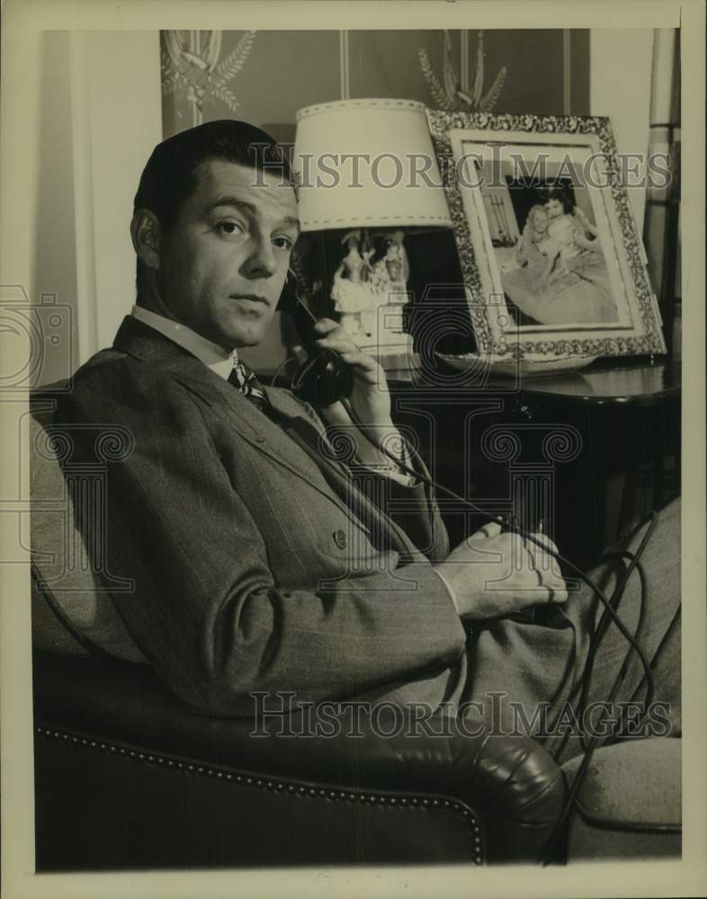 Press Photo Man Sits in Chair, Speaks on Telephone - sap50196