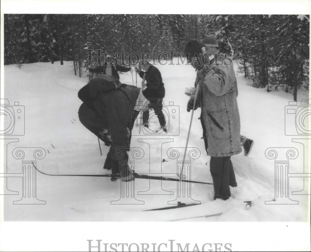 1994 Press Photo Cross country skier bends over to check ski while others rest- Historic Images