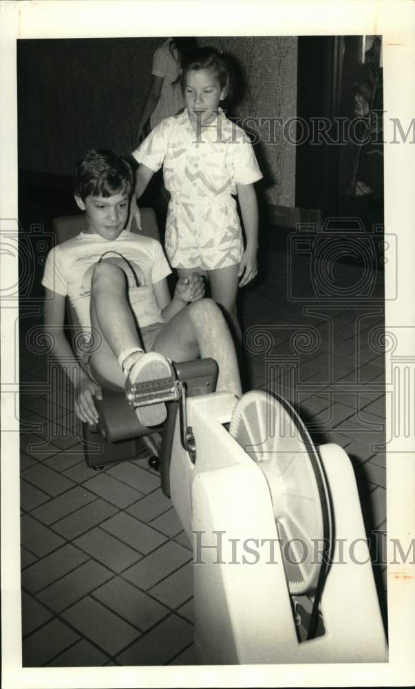 1986 Press Photo Tim Bilbo Riding Exercise Machine at Camillus Mall with Sister- Historic Images