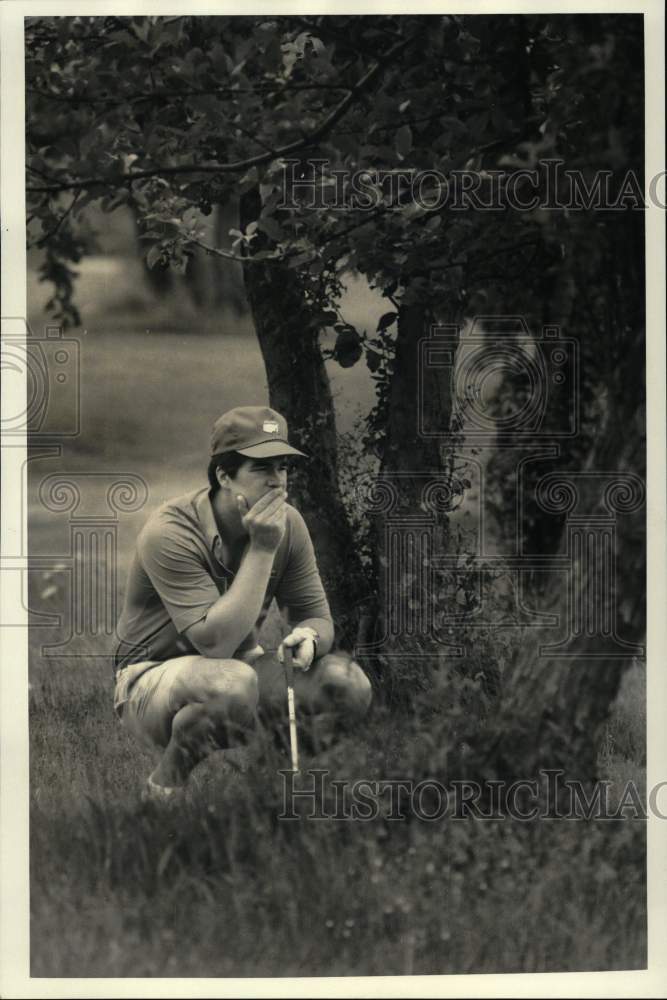 1987 Press Photo Golfer Mike Naton crouches down near a tree on the golf course- Historic Images