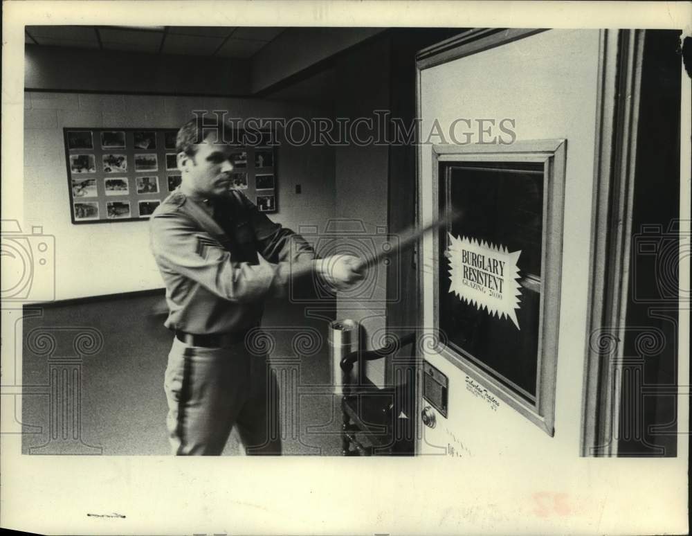 1977 Press Photo New York police officer swings bat at glass panel in Albany