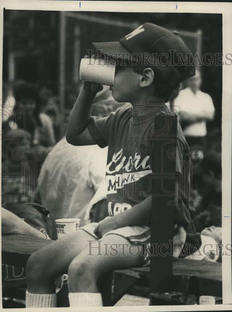 1984 Press Photo Young boy takes a drink from a cup sitting on wooden bench- Historic Images