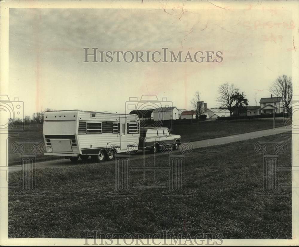 Press Photo Station wagon tows travel trailer on road near rural farm