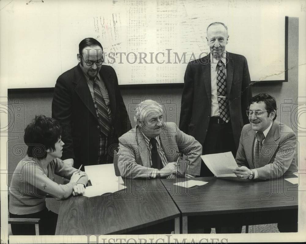 1975 Press Photo Four men and one female sit at tables reviewing papers